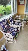 Two rattan chairs with blue floral cushions next to glass top table on porch