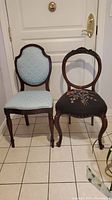 Both vintage chairs visible side by side. One with light blue fabric upholstery, the other with needlepoint seat and open back.