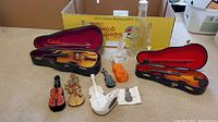 Full lot displayed with two violin-shaped glass perfume bottles in cases, and five small violin-shaped collectible perfume bottles and decorative miniatures on the floor.