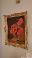 Full view of oil painting showing red poppies in a glass vase, framed in ornate gold wooden frame, hanging on a wall.