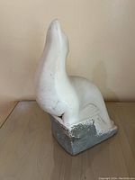 Side view of the white ceramic/plaster sea lion sculpture showing its upright pose and gray base with wear.