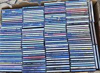 Photo showing multiple stacks of pop music CDs in jewel cases placed inside a cardboard box. Titles are from the 80s and 90s.