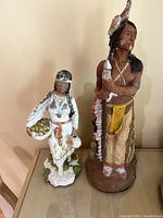 Both Native American chalkware statues shown standing side by side. Warrior on right is taller, Squaw on left smaller with basket.