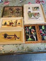 Full overview of 6 framed Mexican street art prints and paintings displayed on floral quilt, showing various themes and frame styles.