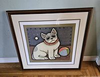 Framed lithograph print of a stylized dog with collar and ball, with visible framing details and room setting.