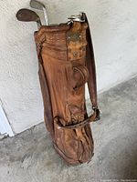 Photo of worn vintage brown leather Burton golf bag standing up, showing detailed embossing and strap