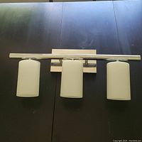 Image showing the chrome bathroom light fixture with three frosted glass shades laid flat on a dark surface.