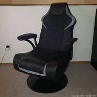 Front view showing black and grey mesh and faux leather surfaces, padded headrest and armrests, round pedestal base