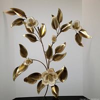 Floral wall hanging showing curved brass leaves and white ceramic flower petals attached to brass stems against a white wall.