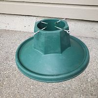 Photo of a green plastic Christmas tree stand with a wide circular base and four adjustable metal screws to hold a tree securely.