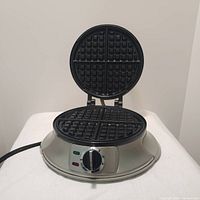 Open view of Cuisinart waffle iron showing 6-inch round cooking griddle with four waffle quadrants and adjustable temperature dial with indicator lights.