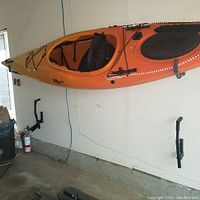 One set of folding kayak holders mounted on a wall with an orange kayak stored on the rack.