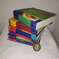 Stacked set of seven Harry Potter books by J.K. Rowling with visible colorful spines. The Dumbledore's Army commemorative coin is placed in front.