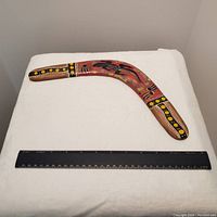 Hand-painted indigenous Australian boomerang with a lizard and symbolic dot patterns, placed next to a ruler showing 12 inches for scale.