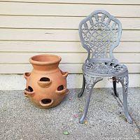 Photo showing the large terracotta strawberry plant pot next to a decorative metal chair for scale.