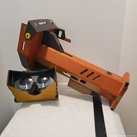 Image of Nintendo Labo VR Toy-Con set includes orange VR blaster and black/orange VR headset made from cardboard with visible lenses.