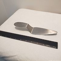 Brushed stainless steel pie serving spatula placed next to a black ruler showing approximate length of 8 inches.