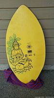 Top side of yellow skimboard with Buddha graphic and logos