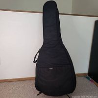 Front view of black Halron soft guitar bag standing upright on carpeted floor with pocket and handle visible.