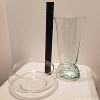 Photo showing two clear glass vases, one tall with flared rim and one short bowl-shaped, on white surface with a ruler to show size.