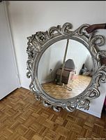 Front view of the large round mirror showing intricate scroll and floral carved pattern on mixed silver and gold finish frame