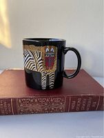 Side view of the black ceramic mug showing the zebra-striped cat design with a red face on one side.