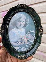 Front view of the vintage oval frame with faux emerald green finish and black and white photo inside showing a young girl holding flowers.