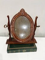 Full front view of the reddish mahogany style oval picture frame on its base with metal swivel knobs on both sides.