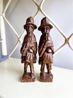 Front view of pair of hand-carved wooden traveler farmers, showing detailed facial features and attire.