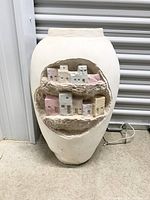 Front view of the large vintage floor vase showing the carved miniature village with pastel colored buildings and rough textured background.