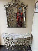 Front view of the marble top side table with intricate metal floral base and matching ornate metal shutter wall mirror.