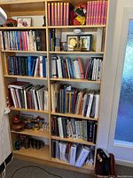 Front and side angle view of the wood shelf unit filled with books and decorative items for display purposes. Shows shelving configuration and size.