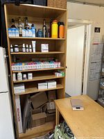 Front view of the wooden shelf unit filled with various items including bottles, boxes, and packages on several shelves.