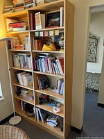 Photo of wood shelf unit filled with books and decorative items for scale. Shelves arranged in two vertical columns with multiple adjustable shelves each.