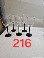 Front angle view of five wine glasses with geometric shapes and black stems on white surface.