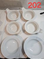 Top view of 6 white china soup bowls consisting of 4 onion soup style bowls with handles and 2 larger round bowls.