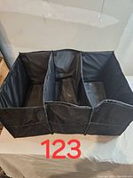 Front view of the car trunk organizer showing three open compartments, black fabric material with mesh sides, slightly dirty from storage.