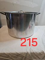 Front view of a large stainless steel stock pot with side handles and matching lid, placed on a white cloth surface.
