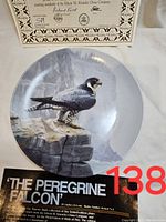 Close-up of the Peregrine Falcon plate showing detailed falcon image and certificate in the background.