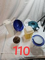 Six vintage Tupperware kitchen containers of various colors and shapes arranged on white fabric background