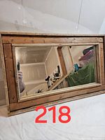 Image of rustic wooden framed mirror with visible wood grain and imperfections in the frame, leaning against a wall.