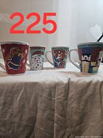 Four Christmas-themed coffee mugs in a row showing all designs: angel, snowman, reindeer, nutcracker soldier