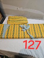 Two bolts of yellow soft jersey knit fabric with green geometric and floral patterns, one folded and one rolled and tied.