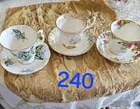 Three vintage Royal Albert tea cups with matching saucers displayed on patterned brown and white fabrics, showing varied floral designs.