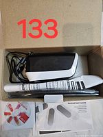 Open box showing the black and white film scanner device, white pen-like tool, USB cable, software CD, and quickstart guide.