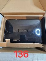 Top view of the black Netgear wireless router inside its open cardboard box, showing the NETGEAR logo on top.