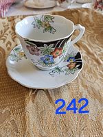 Side view of the vintage handpainted china tea cup with floral pattern and matching saucer on a gold textured cloth.