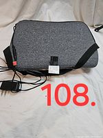 Front view of the grey textured massage cushion with attached power adapter and adjustable strap laid on a white surface.