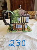 Side view of the hand painted Ye Olde Inne teapot showing intricate design of the house with a window and door detail, tree trunk handle, and textured roof.