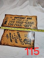 Two vintage wooden wall plaques shown side by side on a white cloth background with measuring tape indicating size, plaques have burnt edges and painted text.
